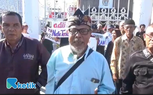 Foto Warga Desa Bulupayung Kesugihan melakukan aksi unjuk rasa dengan membentangkan poster berisikan tuntutan mereka. (Foto: Nani Eko/Ketik)