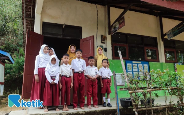 Foto Siswa-siswi SDN 3 Gunungsari berfoto bersama para guru di depan ruang kelas. Sekolah dasar negeri yang berada di pelosok ini bertahan dengan jumlah murid yang kian menyusut dan infrastruktur yang minim, mulai dari akses jalan hingga ketersediaan air dan listrik. (Foto: Al Ahmadi/Ketik)
