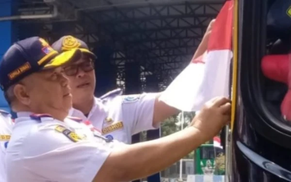 Foto Kadishub Jatim Nyono memasang bendera merah putih di dekat spion bus di Terminal Kertajaya, Mojokerjo. (Foto: Dishub Jatim for Ketik.com)