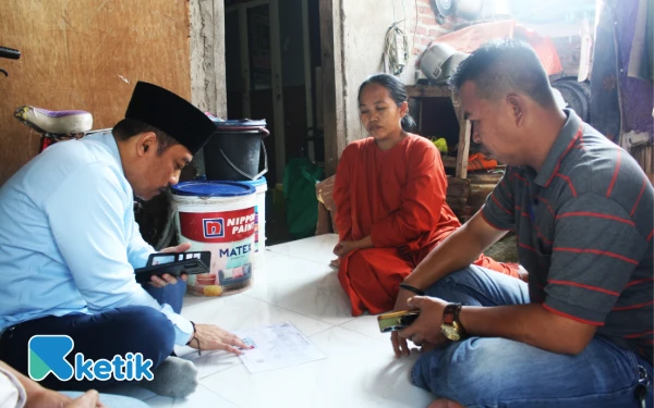 Foto Anggota DPRD Sidoarjo Dhamroni Chudlori memeriksa kartu keluarga dan KTP keluarga Erna Sri Wahyuni sambil duduk di lantai rumah Desa Lambangan, Kecamatan Wonoayu, pada Jumat (29 Agustus 2025). (Foto: Ketik.com)