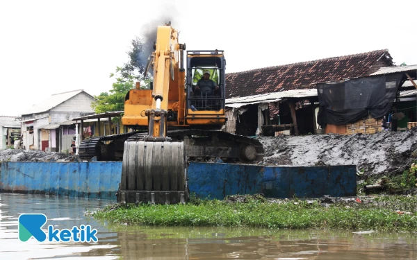 Foto Alat berat ekskavator mengangkat lumpur dari dasar Sungai Mbah Gepuk ke pinggir sungai. (Foto: Fathur Roziq/Ketik.com)