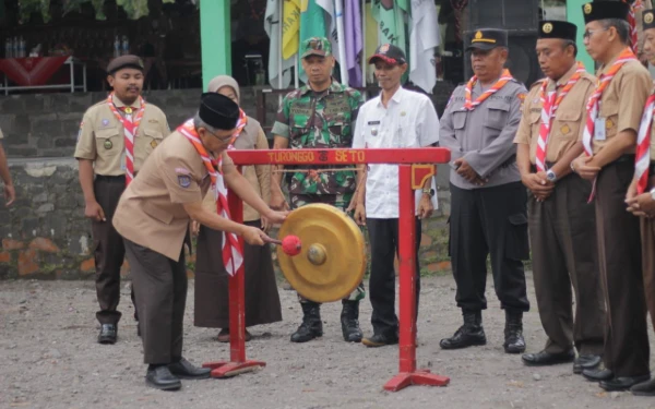 Foto Sekda Sleman memukul gong menandai dimulainya acara secara resmi. Sebuah momen persatuan dengan kehadiran pejabat, TNI, dan Polri, memberikan dukungan penuh kepada generasi muda Pramuka. (Foto: Prokompim Sleman for Ketik.com)
