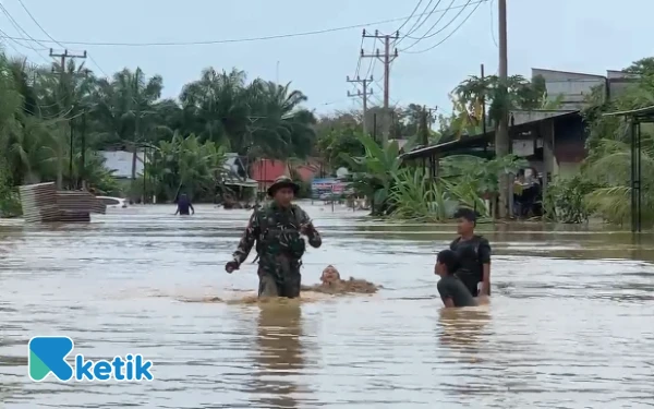 Foto Anak-anak bermain air dan melihat seorang personel TNI di tengah arus banjir bandang di Jalan Nasional, Kuta Trieng, Nagan Raya, Kamis, 27 November 2025. (Foto: T. Rahmat/Ketik)