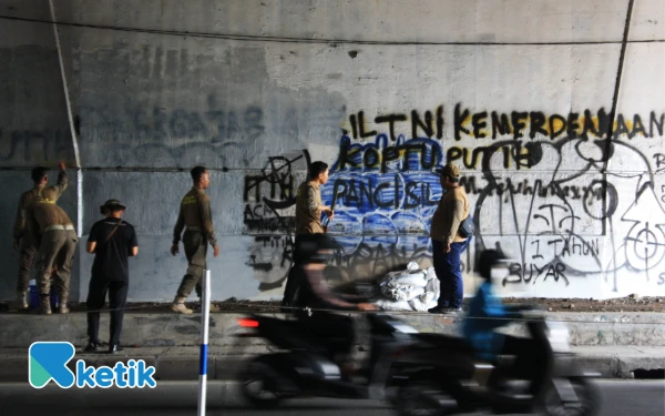 Foto Personel Satpol PP Sidoarjo dan DLHK Sidoarjo saling bantu membersihkan bekas-bekas coretan di dinding jembatan tol Jalan Raya Jati. (Foto: Fathur Roziq/Ketik.com)