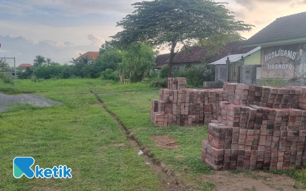 Foto Kondisi sisi barat Stadion Forlantas, Sidomoyo, Godean, Sleman, pada Rabu sore, 17 Desember 2025. Di lokasi ini terlihat tumpukan material paving blok dan upaya pembuatan lubang untuk pemasangan pembatas jalur joging track yang hingga kini belum diketahui asal-usul anggarannya. (Foto: Fajar Rianto/Ketik.com)