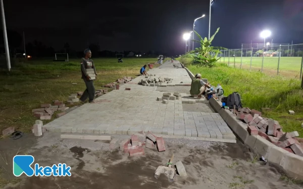 Foto Aktifitas penataan pasir dan pemasangan pembatas beton (kanstin)  ldan paving blok di sisi timur Stadion Forlantas, Sidomoyo, Godean, Sleman, Jumat malam 19 Desember 2025. Proses pembangunan joging track ini sempat menjadi pertanyaaan masyarakat karena ketiadaan papan nama proyek pada awal pengerjaannya, serta sepi aktifitas tenaga kerja. (Foto: Fajar Rianto/Ketik.com)