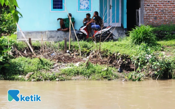 Foto Beberapa warga duduk santai di atas bantaran sungai yang juga mulai longsor. (Foto: Fathur Roziq/Ketik.com)