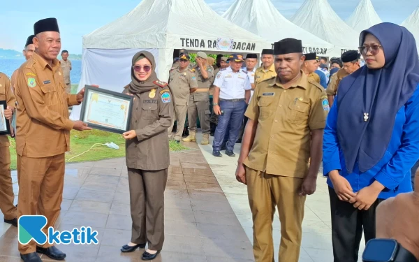 Foto Sekretaris Daerah Safiun Radjulan saat menyerahkan piagam ke Susi Susilawaty Kamarullah, SE, M.Si salah satu penerima penghargaan dari Satuan Polisi Pamong Praja Senin 29 Desember 2025 (Foto: Mursal/Ketik.com)