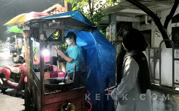 Foto Pelanggan yang bernama Acha (kanan), memesan salah satu menu nasi goreng Gerobak Setan yang terletak di Jl. Jemur Wonosari, Wonocolo pada Selasa tanggal 10 Februari 2026. Mahasiswa semester 4 tersebut menyukai nasi goreng Gerobak Setan karena rasanya yang khas rumahan mengingatkan masakan ibunya. 
(Foto: Kahila/Ketik.com)