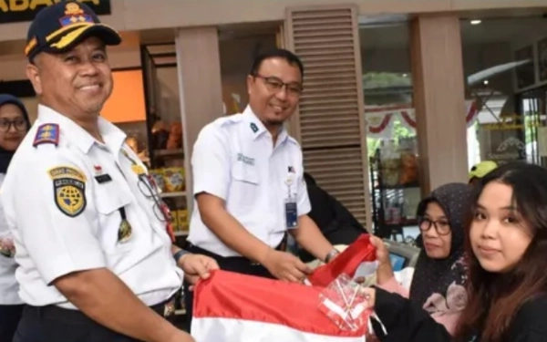 Foto Kadishub Jatim Nyono (kiri) membagikam bendera kepada calon penumpang kereta api di Stasiun Gubeng Surabsya. (Foto: Dishub Jatim for Ketik.com)