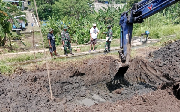 Foto Personel Koramil 13/Seyegan Kodim 0732/Sleman bersama warga menyaksikan pengerjaan awal pembangunan Jembatan Gantung Garuda di Sungai Krusuk, Padukuhan Klangkapan 2, Margoluwih, Seyegan, Sleman, Sabtu, 17 Januari 2026. Sebuah alat berat dikerahkan untuk melakukan pengerukan tanah guna menyiapkan fondasi jembatan. (Foto: Pendim 0732/Sleman for Ketik.com)