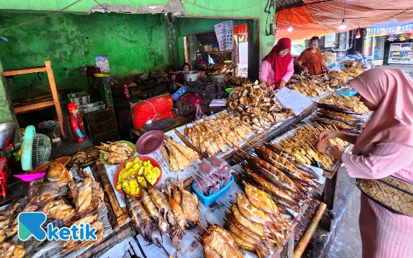Thumbnail Seorang pedagang dan pembeli ikan asap  di kawasan Pantai Kenjeran Surabaya, MInggu, 26 Oktober 2025. Sejumlah jenis ikan asap di antaranya Manyung, Patin, Tuna, Gurami, Ikan Pe, Telur Ikan, dan lainnya. (Foto: Fiqih Arfani/ketik.com)