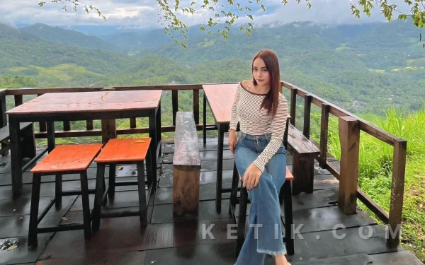 Foto Seorang pengunjung berpose di teras kayu kawasan Pasar Geneng, dengan latar panorama perbukitan hijau yang membentang luas saat pagi hari.