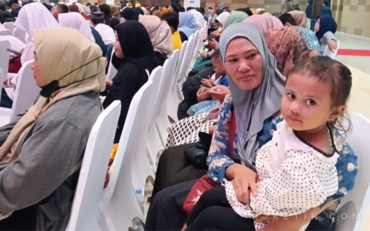 Foto Nurjannah, ibu tunggal asal Desa Sepande, mengantar putrinya, Erlita Arsita, untuk menerima beasiswa anak yatim sambil menggendong anak bungsunya, Aira. (Foto: Fathur Roziq/Ketik.com)